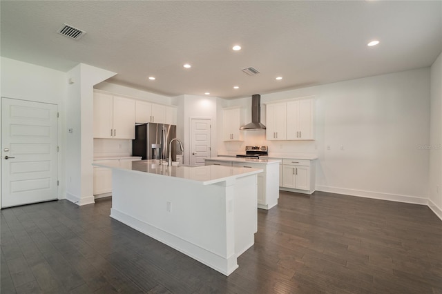 kitchen with a kitchen island with sink, stainless steel appliances, wall chimney exhaust hood, and dark hardwood / wood-style flooring