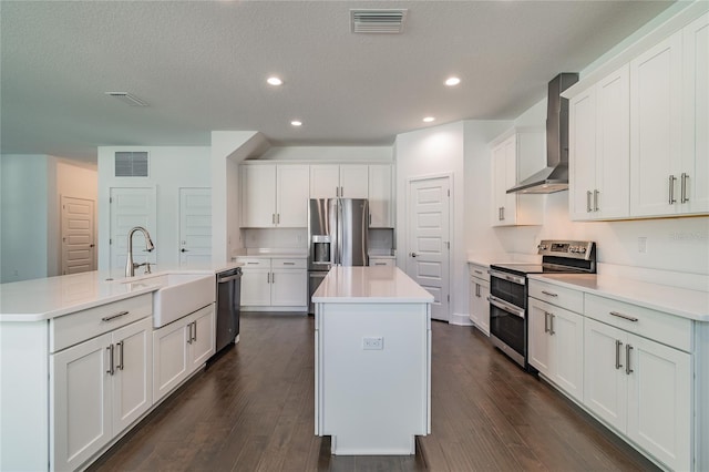 kitchen featuring dark wood-type flooring, wall chimney exhaust hood, a kitchen island with sink, appliances with stainless steel finishes, and sink