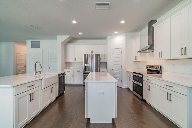 kitchen featuring wall chimney range hood, appliances with stainless steel finishes, a sink, and an island with sink