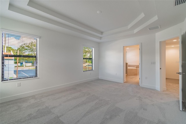 unfurnished bedroom with light carpet, connected bathroom, and a raised ceiling