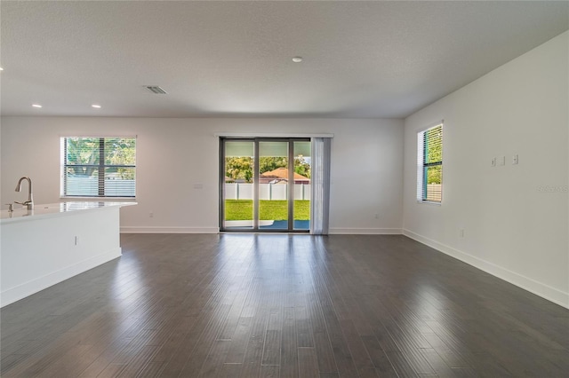 unfurnished living room featuring a sink, recessed lighting, baseboards, dark wood-type flooring, and visible vents