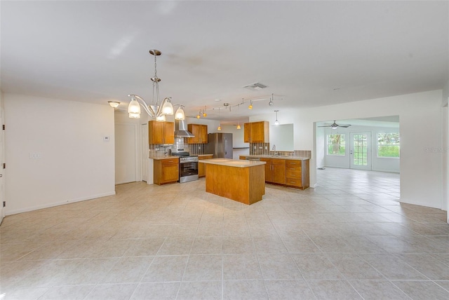 kitchen featuring appliances with stainless steel finishes, tasteful backsplash, wall chimney exhaust hood, ceiling fan with notable chandelier, and pendant lighting