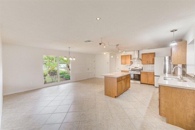 kitchen with wall chimney range hood, sink, decorative light fixtures, a kitchen island, and stainless steel appliances