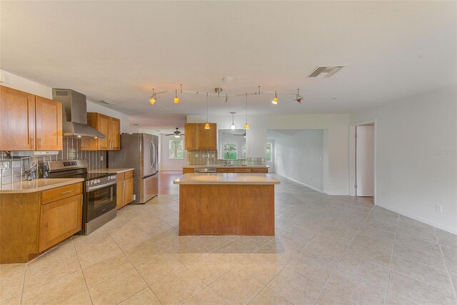 kitchen with decorative backsplash, appliances with stainless steel finishes, ceiling fan, wall chimney range hood, and pendant lighting