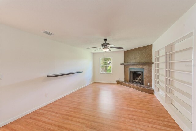 unfurnished living room with ceiling fan, a large fireplace, and light wood-type flooring