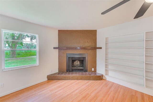 unfurnished living room with a tiled fireplace, ceiling fan, hardwood / wood-style floors, and built in features