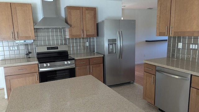 kitchen featuring light tile patterned flooring, wall chimney range hood, appliances with stainless steel finishes, and tasteful backsplash