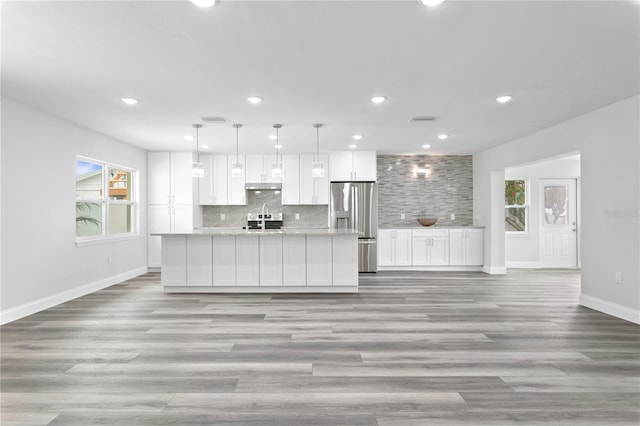 kitchen featuring white cabinetry, hanging light fixtures, stainless steel appliances, light hardwood / wood-style floors, and a kitchen island with sink