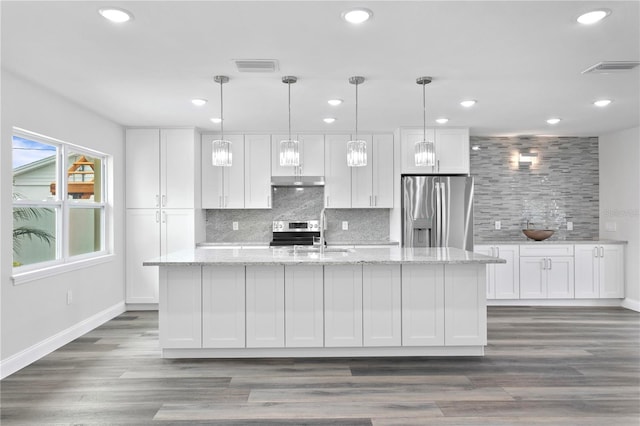 kitchen with light stone counters, white cabinets, stainless steel appliances, and an island with sink