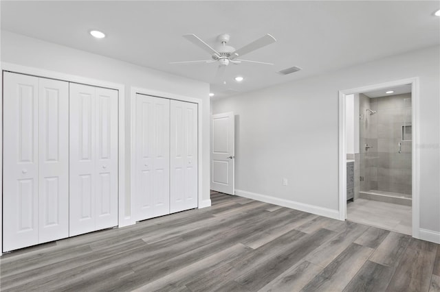 unfurnished bedroom featuring connected bathroom, ceiling fan, light hardwood / wood-style flooring, and multiple closets