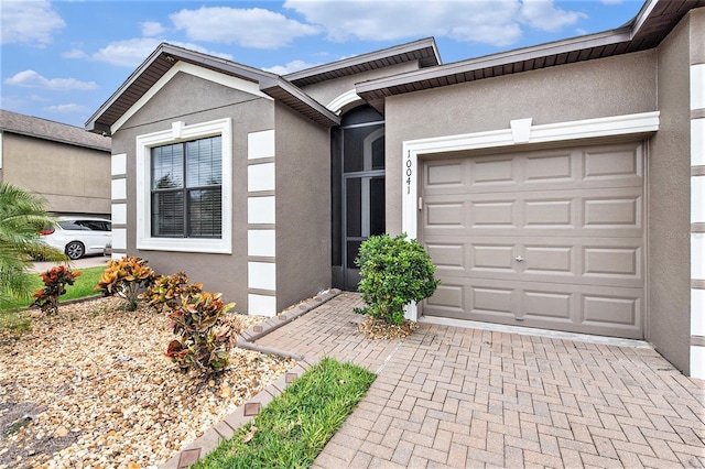 view of front of property with decorative driveway, an attached garage, and stucco siding