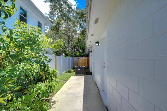 view of home's exterior with central AC unit, concrete block siding, and fence