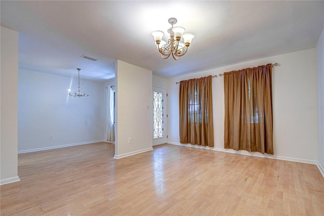 spare room with light wood-type flooring, visible vents, a chandelier, and baseboards