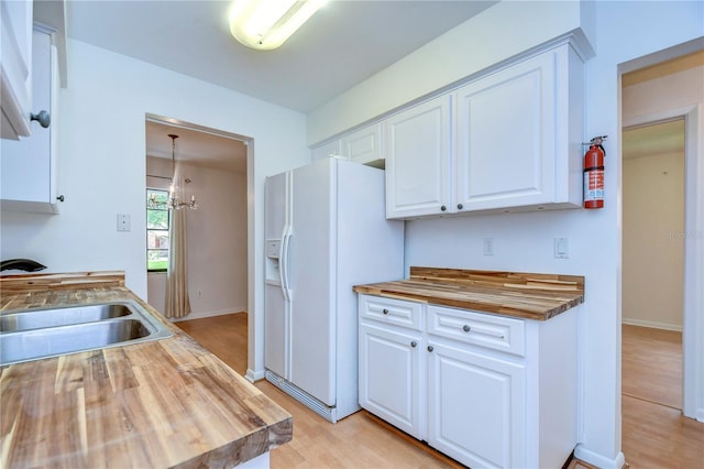 kitchen featuring white refrigerator with ice dispenser, white cabinets, a sink, butcher block countertops, and light wood-type flooring