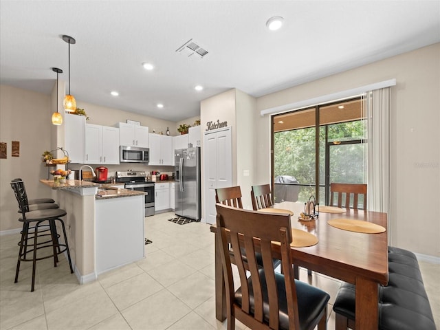 kitchen featuring sink, dark stone countertops, light tile patterned floors, stainless steel appliances, and kitchen peninsula