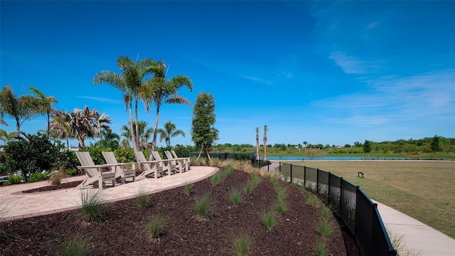 view of home's community with a patio area, fence, a water view, and a lawn