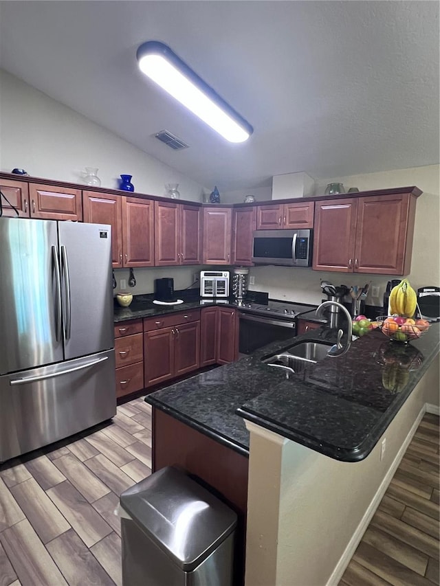 kitchen featuring light hardwood / wood-style flooring, sink, kitchen peninsula, lofted ceiling, and stainless steel appliances