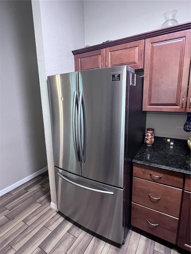 kitchen with light wood-type flooring, stainless steel refrigerator, and dark stone countertops