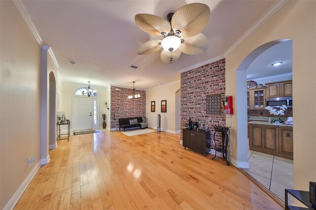 living room featuring light wood-type flooring, ceiling fan with notable chandelier, a fireplace, and ornamental molding