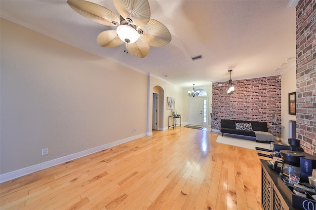 living area featuring arched walkways, ceiling fan with notable chandelier, visible vents, wood-type flooring, and crown molding