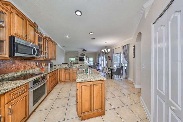 kitchen with crown molding, light tile patterned floors, a kitchen island, light stone countertops, and appliances with stainless steel finishes