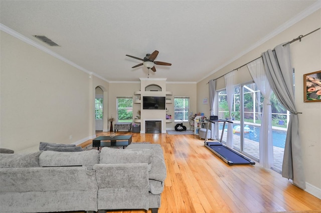 living room featuring arched walkways, crown molding, a fireplace, visible vents, and hardwood / wood-style floors