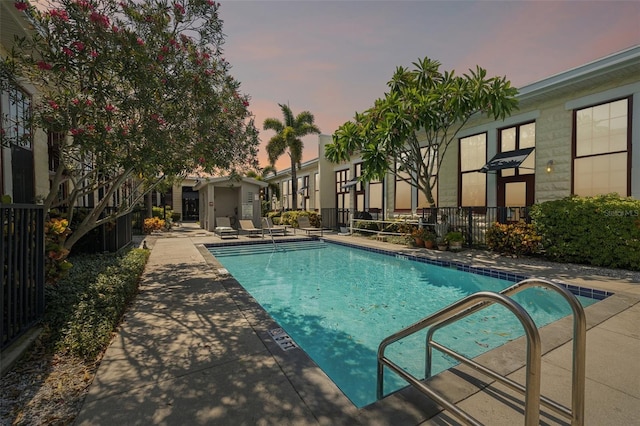 pool at dusk featuring a patio, fence, and a community pool