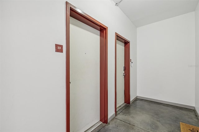 hallway featuring baseboards and concrete flooring