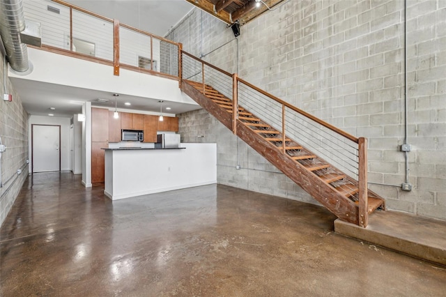 unfurnished living room featuring concrete flooring, concrete block wall, stairway, and a high ceiling