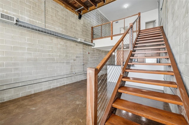 staircase with visible vents, concrete floors, a towering ceiling, and concrete block wall