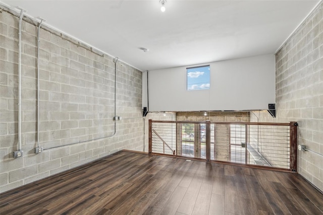 unfurnished room featuring concrete block wall and dark wood finished floors