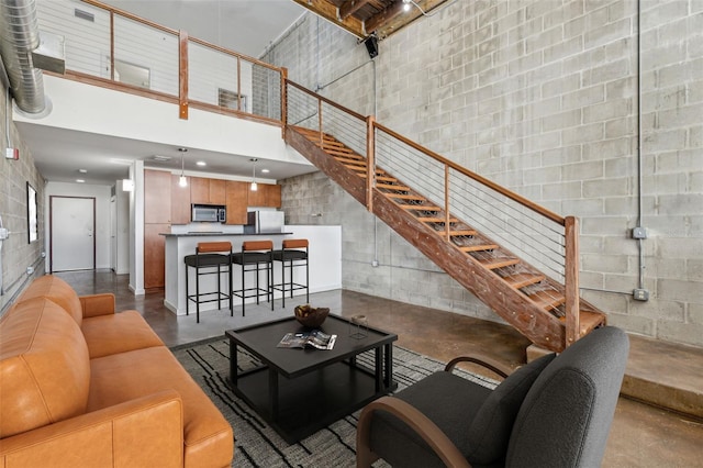 living room with stairway, concrete block wall, concrete floors, and a towering ceiling