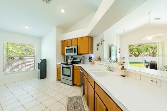 kitchen with lofted ceiling, appliances with stainless steel finishes, brown cabinets, and a sink