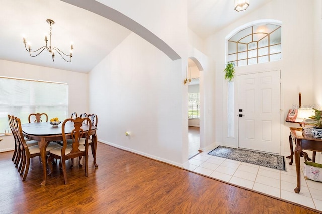 foyer with arched walkways, high vaulted ceiling, a notable chandelier, wood finished floors, and baseboards