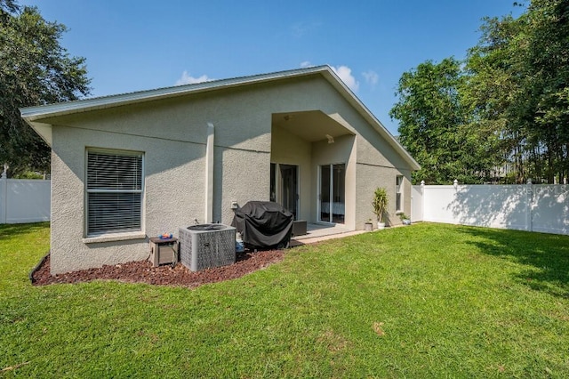 back of property featuring a yard, cooling unit, fence private yard, and stucco siding