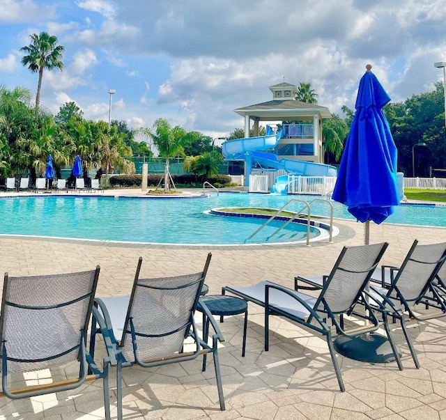 pool featuring a water slide, a patio area, and fence