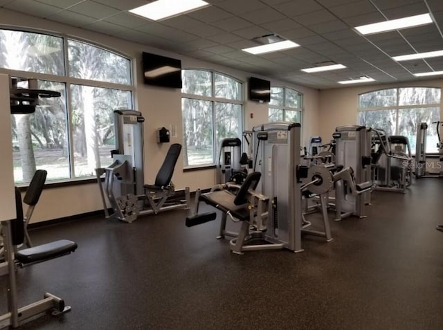 gym with a paneled ceiling and baseboards