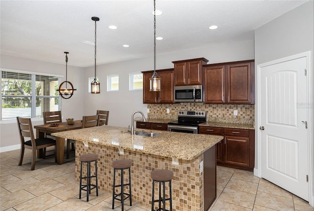 kitchen with appliances with stainless steel finishes, a kitchen island with sink, sink, hanging light fixtures, and a breakfast bar area