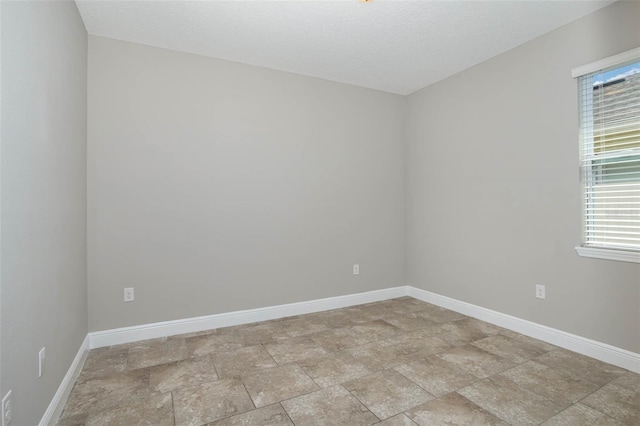 spare room featuring stone finish floor, a textured ceiling, and baseboards