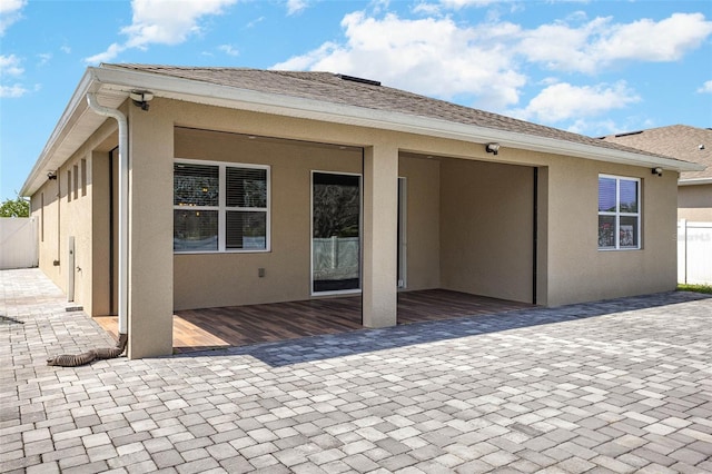 rear view of house featuring a shingled roof, fence, a patio, and stucco siding