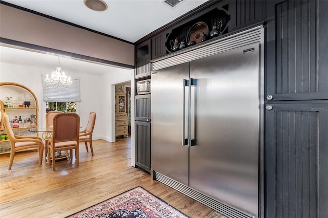 kitchen featuring light wood-type flooring, hanging light fixtures, built in refrigerator, a notable chandelier, and crown molding