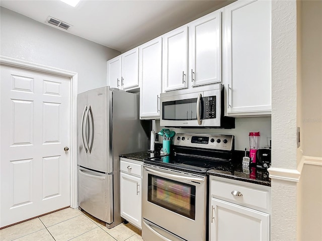 kitchen with light tile patterned floors, appliances with stainless steel finishes, dark stone counters, and white cabinets