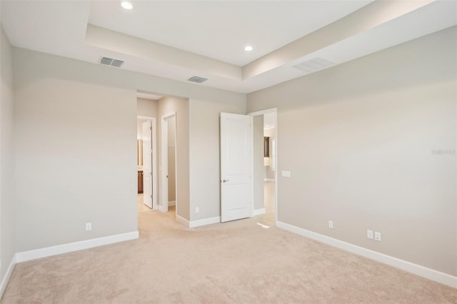 spare room featuring a tray ceiling and light carpet