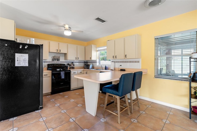 kitchen with ceiling fan, decorative backsplash, a breakfast bar, kitchen peninsula, and black appliances