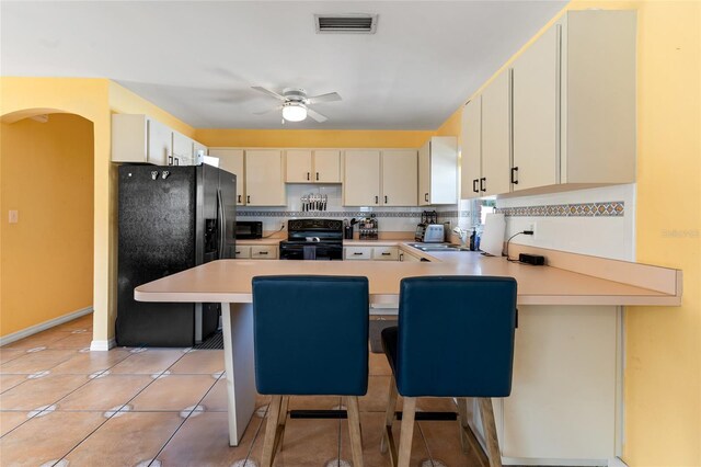 kitchen with backsplash, ceiling fan, light tile patterned floors, kitchen peninsula, and black appliances