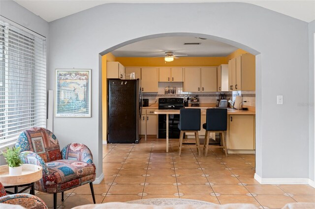 kitchen featuring black electric range oven, freestanding refrigerator, light countertops, backsplash, and light tile patterned flooring