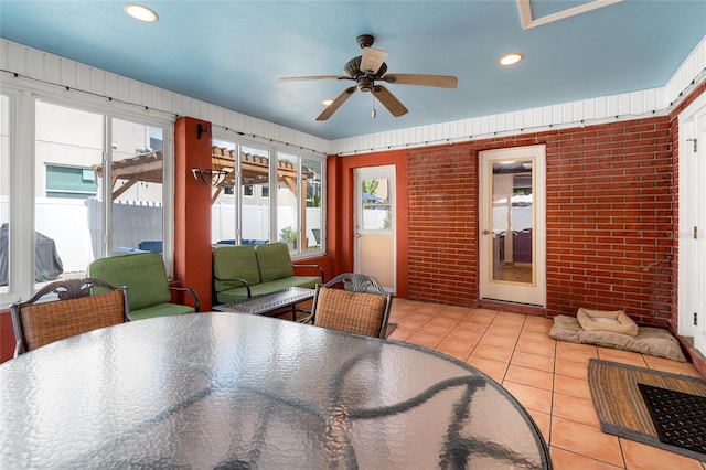 tiled dining area featuring ceiling fan and brick wall