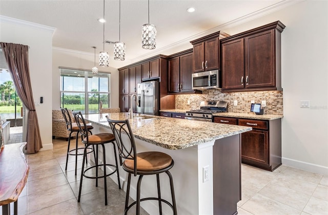 kitchen with a center island with sink, backsplash, a kitchen bar, hanging light fixtures, and stainless steel appliances