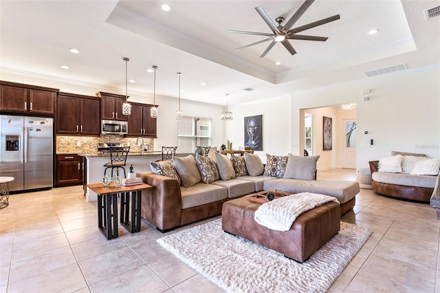 tiled living room with ceiling fan, ornamental molding, and a tray ceiling