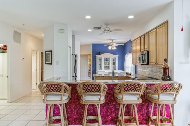 kitchen featuring a kitchen breakfast bar, appliances with stainless steel finishes, tasteful backsplash, kitchen peninsula, and ceiling fan